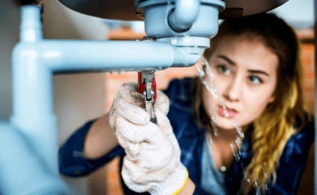 A plumber tightening a fitting under a sink